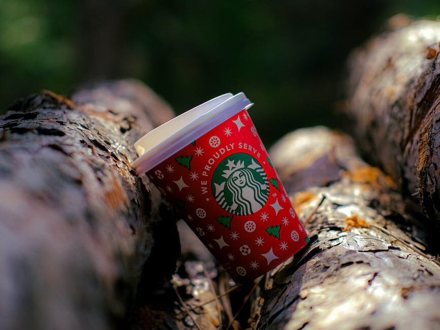 red disposable starbucks coffee cup lying on a stack of wood logs